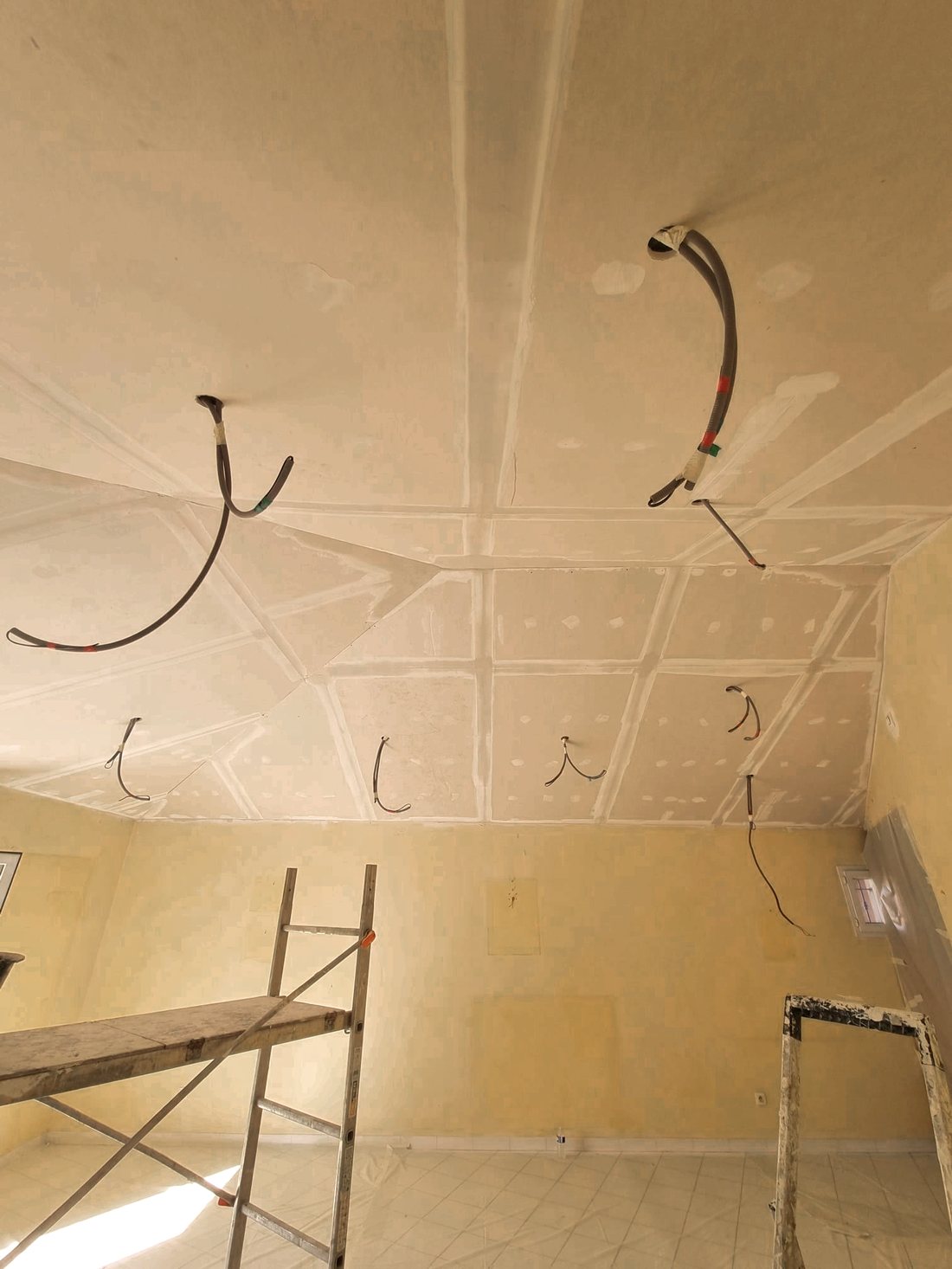Plafond en plaques de plâtre en cours de finition, fils électriques en attente