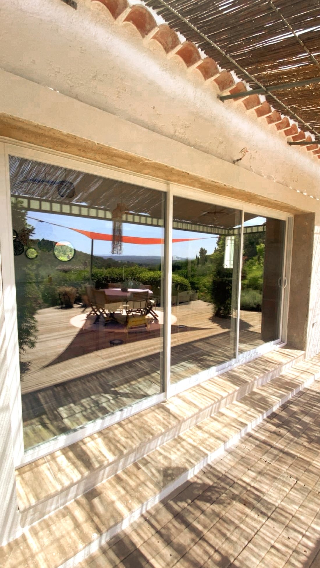 Baie vitrée coulissante aluminium blanc posée sous une pergola provençale